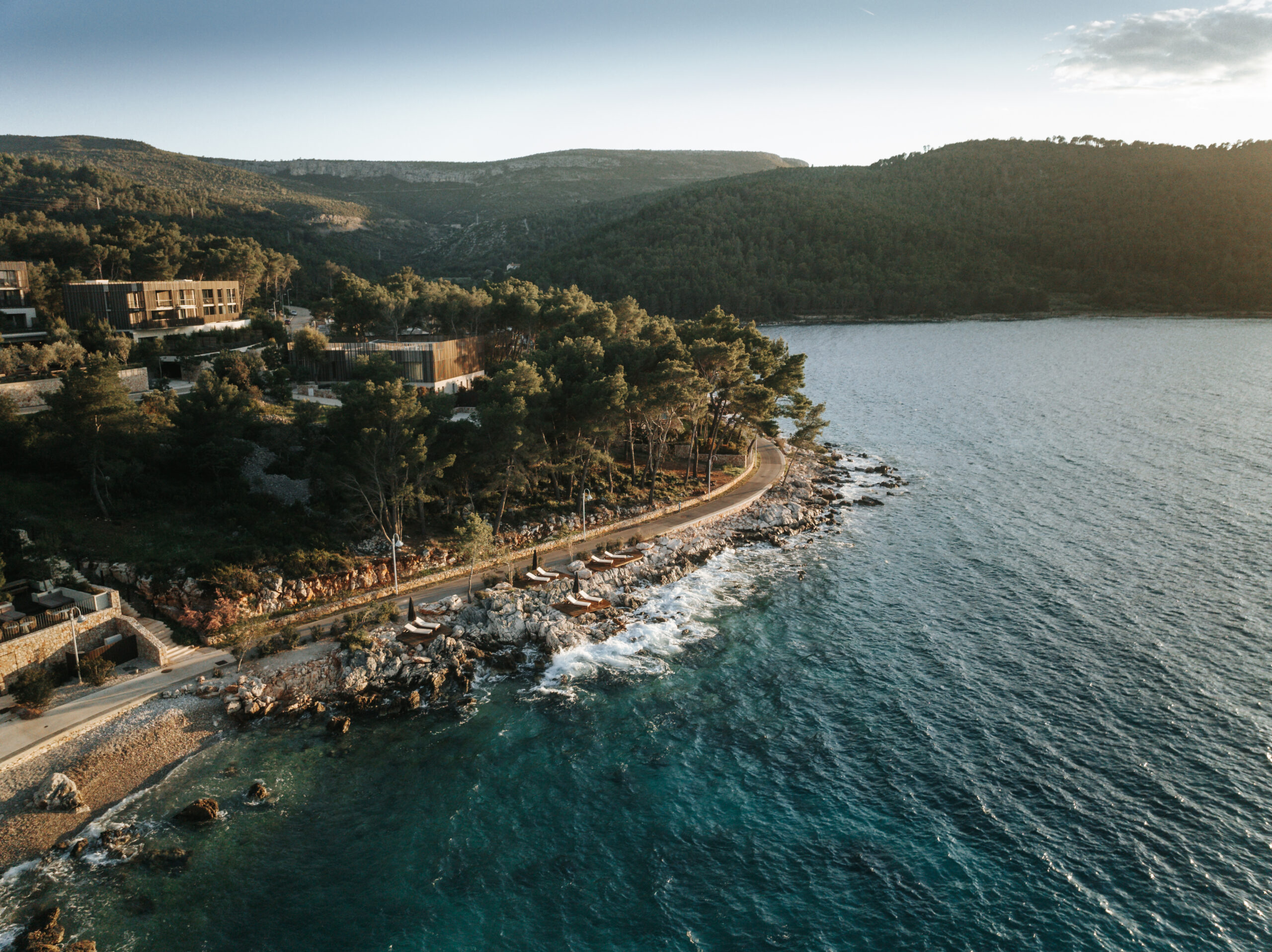 02_Maslina Resort_LIFESTYLE_Aerial view_2023 View of the Adriatic Sea from the shore at Maslina Resort, with clear blue water, rocky coastline, and pine trees in the background.